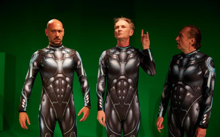 Drei Männer in futuristischen Rüstungen stehen in einem Green-Screen-Studio