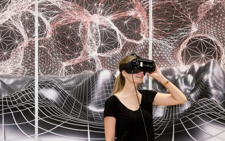 Two women with VR glasses stand in front of a graphic landscape
