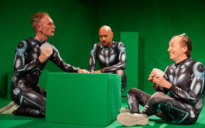 Three men in futuristic armor play cards in a green-screen studio