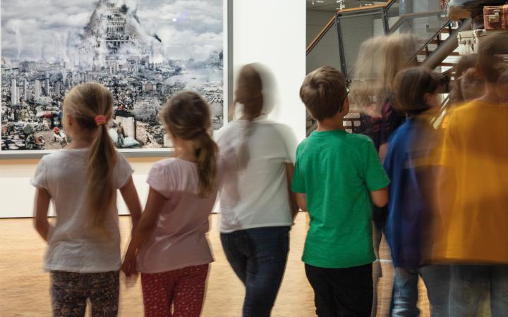 Zu sehen sind eine verschommene Gruppe Kinder vor einem Bild, welches den Turm zu Babel zeigt.