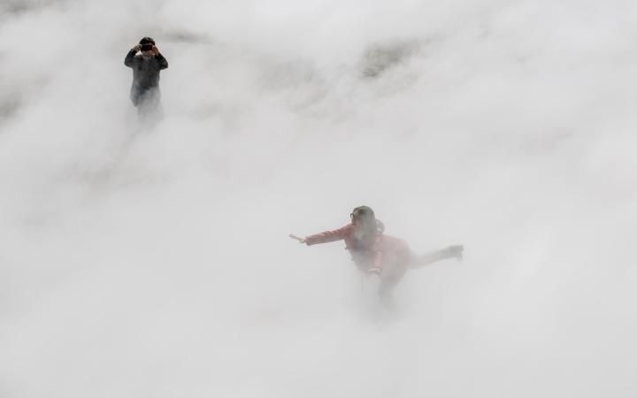 You can see a woman balancing on one leg with outstretched arms, half hidden in the fog.