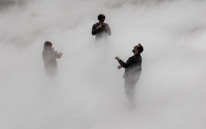 The photo shows three laughing people standing in a thick cloud of fog.