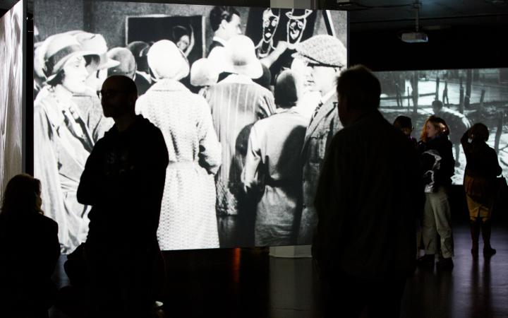 The photo shows the exhibition room with a large projection of a black and white film.