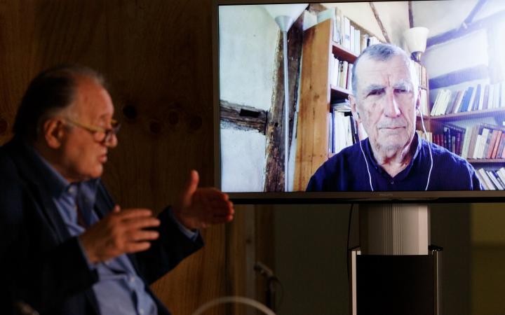 Peter Weibel sits in front of a large screen on which Bruno Latour can be seen.