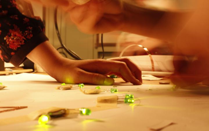 One can see a hand, that is leaning on a table on which - taped to a sheet of paper - green LEDs are glowing.