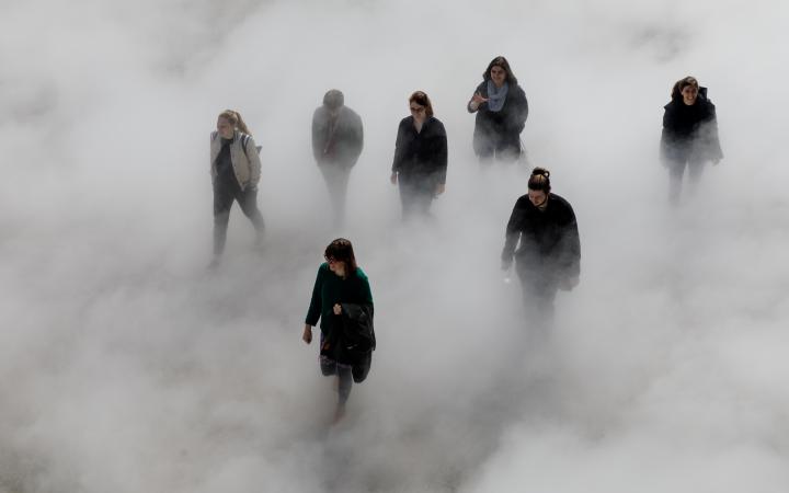 The photo shows seven laughing people walking across the Human Rights Square, partly covered by fog.