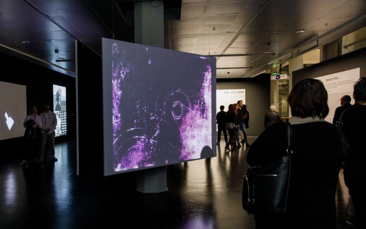 Foto von Menschen vor einer Leinwand mit einem abstrakten Video in Lila – Eine Impression der Ausstellung »bauhaus.film.expanded« am ZKM Karlsruhe.