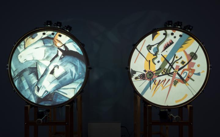 You can see two standing drums, each showing a picture of different shapes on the round surface. On the left drum a horse's head is recognizable from the forms. 
