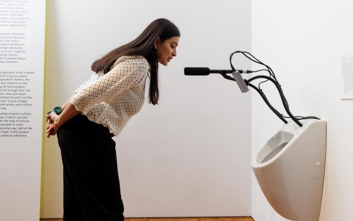You can see a person speaking into a microphone. The microphone is attached to a toilet.
