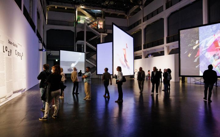 Ausstellungsansicht von »Soun-Gui Kim: Lazy Clouds« am ZKM | Karlsruhe, 2022. Mehrere große Bildschirme hängen verteilt im Raum von der Decke.