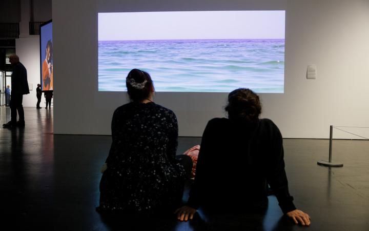 You can see two people sitting in front of a screen. On the picture you can see the sea.