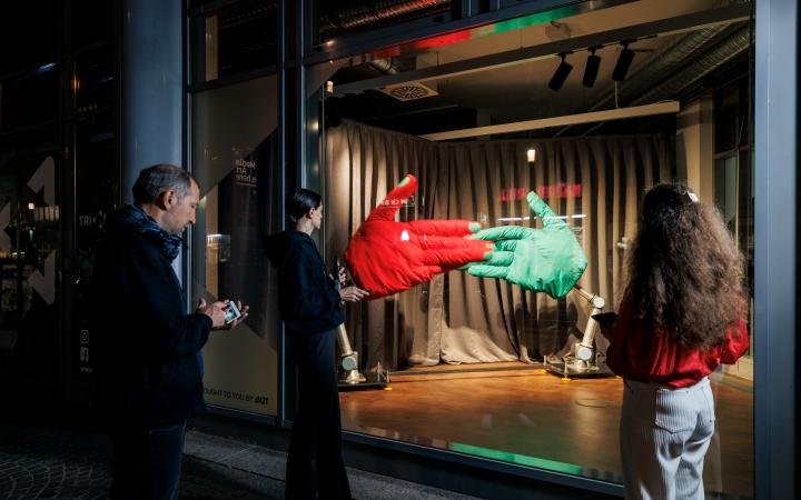 On the picture you can see the instalation "Handshake", AATB (Andrea Anner, Thibault Brevet), in the triangle at Kronenplatz. A big ror and big green hand are fixed on the ground and hit each other. Several people are standing in front of the window.