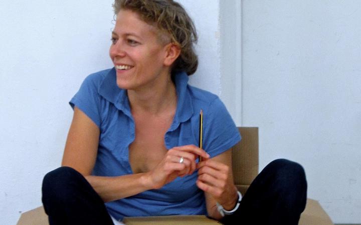 Anja Konjetzky sitzt lässig in einem Pappkarton und hält einen Bleistift in der Hand. 