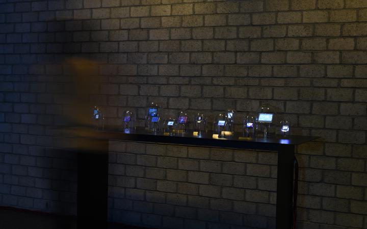 The photo shows a dark table with several glass bells with integrated displays are exposed. A person is blurred on the left side.