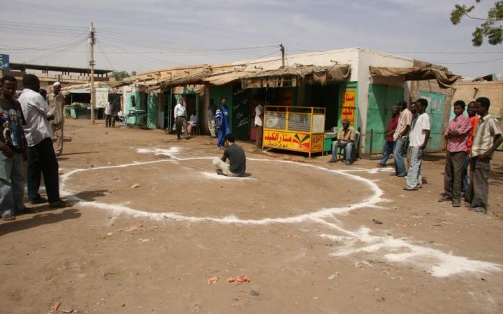 Künstler Barış Seyitvan sitzt innerhalb eines auf dem Boden aufgemalten weißen Kreises in einem sudanesischen Dorf.