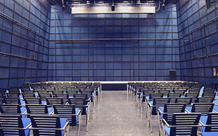 Picture of ZKM Media Theatre with chairs in a row and stage. Modern architecture with a basic wall colour in blue.