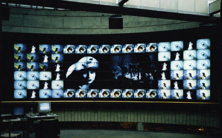 The photo shows a large screen that is composed of many smaller screens and thus shows a large image. That of a young woman looking into the camera