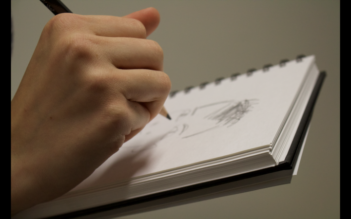 Eine Hand zeichnet etwas auf einem Block Papier. 