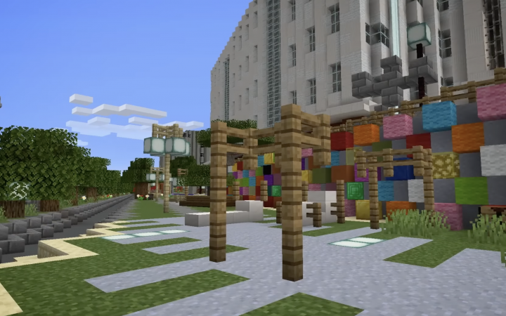 Minecraft view of a representation of the urban space. House facades are shown in the background. A wall of coloured and grey blocks is located in the middle ground. A playground is shown in the foreground.