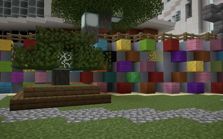 Minecraft view of a representation of the urban space. A tree is shown in the centre of the image. Behind it is a wall in grey and coloured blocks.