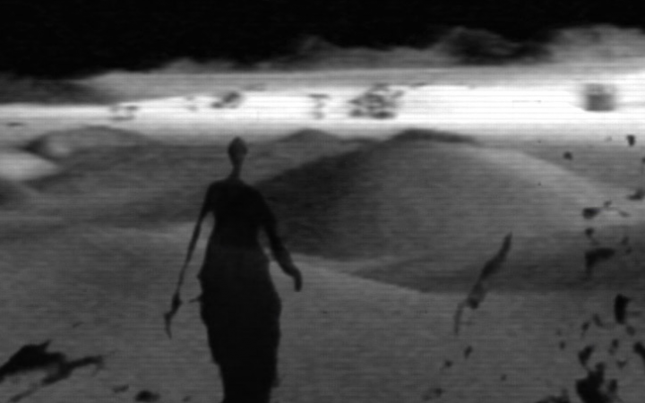Das Bild ist in schwarz-weiß, eine schattenhafte Gestalt wandert durch die Wüste