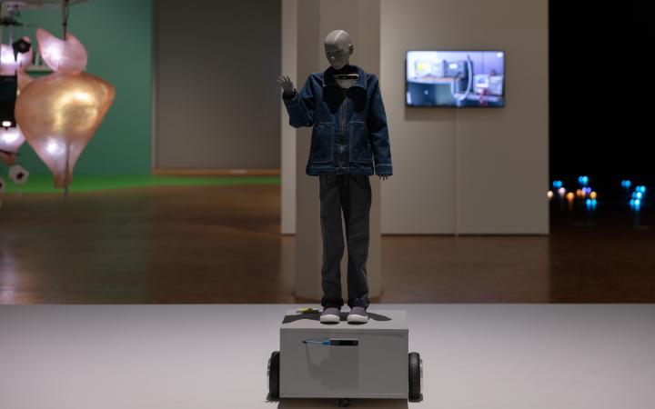 In the picture there is a human-like robot raising his hand. He is wearing jeans clothes.