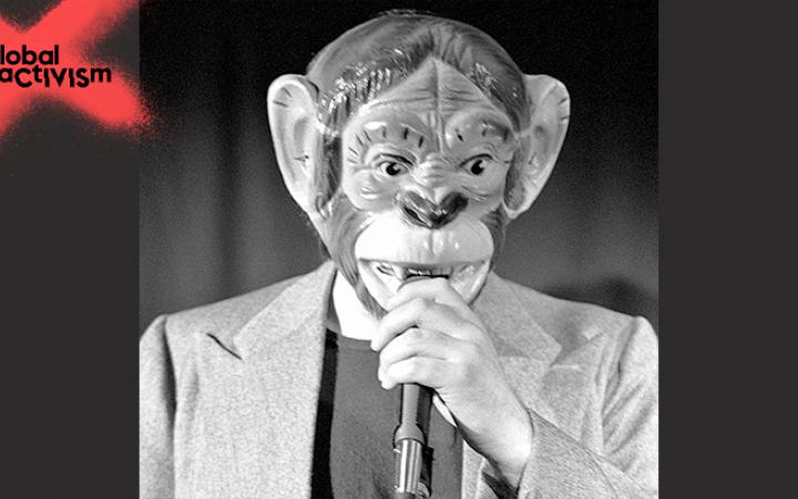 Ein Mann mit einer Affenmaske spricht in eine Mikrofon