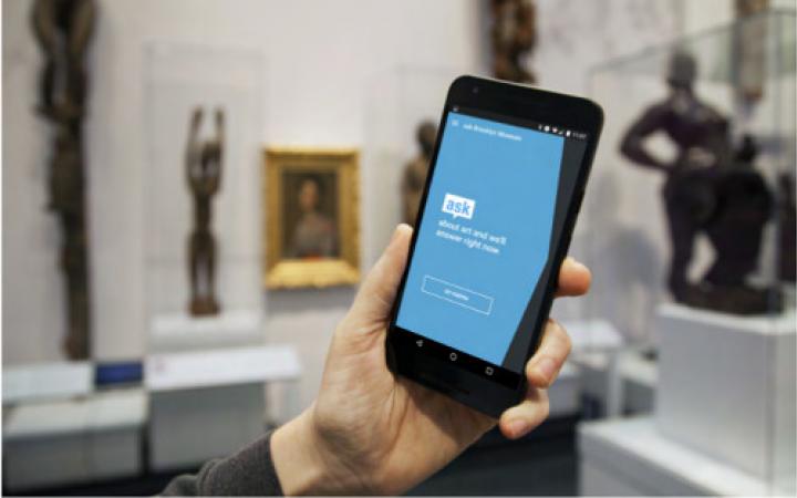 Mobiltelefon in der Hand eines Museumsbesuchers. Auf dem Bildschirm wird der Museumsbot ASK gestartet.