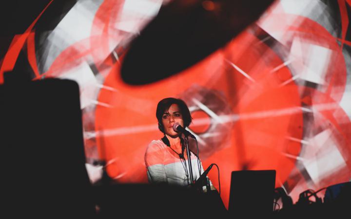 A woman at the microphone, in front of her red-white light projections.