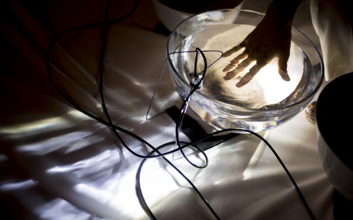 Photo of a hand in a glass bowl filled with water. A microphone is hanging in the bowl.