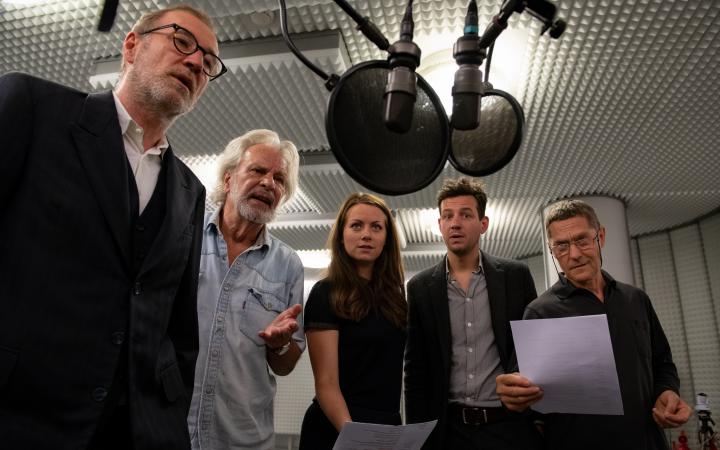 5 Personen stehen in einem Soundstudio vor einem Mikrofon