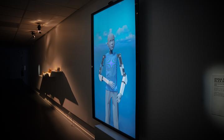 Anna Dumitriu & Alex May, »Cyberspecies Proximity Digital Twin«, 2020. Zu sehen ist ein humanoider digitaler Roboter auf einem Bildschirm vor einem blauen Hintergrund.