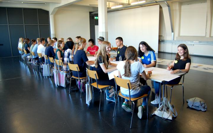 Many young pupils sit at a table within the framework of an event of the cultural academy.