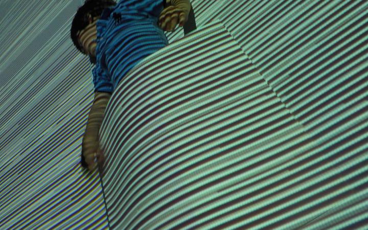 A boy in front of a wall with projections. In front of him there is a big piece of paper and it seams as though the boy is tucked into the projection.