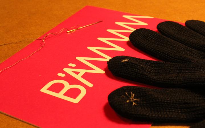 A glove with conductive thread at the fingertips is lying on the table next to a BÄM-flyer