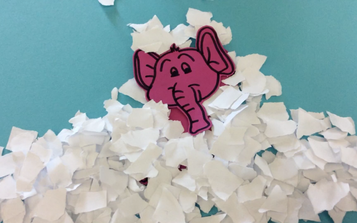 A still out of an stop motion movie with a pink elephant that is covered with shreds of paper, that make him look like he is stuck in snow. 