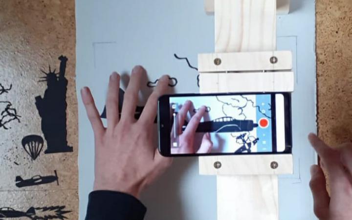 The image shows a hand, various materials and stencils, and a mobile device as a close-up. The image was created as part of the Cultural Academy Baden-Württemberg 2020/21.