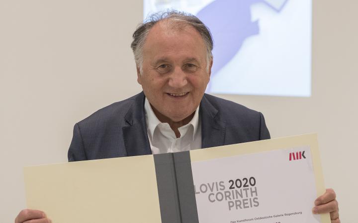 A photo of the artist, curator and ZKM director Peter Weibel, holding the Lovis-Corinth Prize in his hands in the form of a certificate.