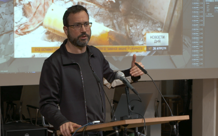 Eyal Weizman, ein Mann mit Bart und Brille hält einen Vortrag vor einer Leinwand..