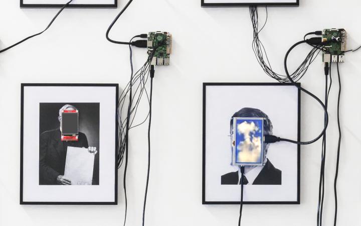 Das Foto zeigt vier eingerahmte Portraits auf deren Gesichter kleine Monitore angebracht sind.