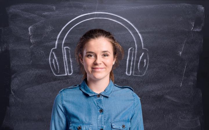 A woman is standing in front of a blackboard with headphones painted on.