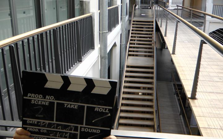 There are little hands of a child visible, they are holding a clapperboard for movies. In the background we can see stairs within the zkm.