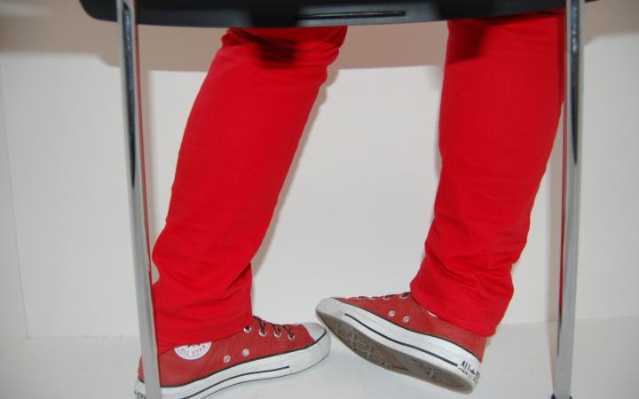 Picture of a photosafari: metal chairlegs and legs and feet of a child that is wearing red sneakers and pants.
