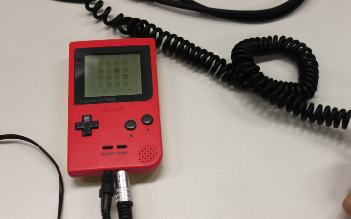 A red gameboy lies on the table and around that some cables.