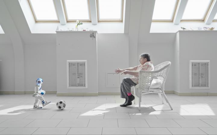 A small humanoid robot plays soccer with a senior citizen in a nursing home.