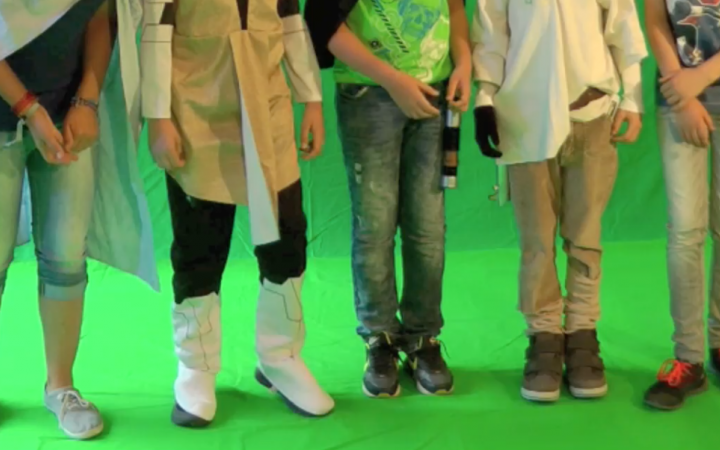 Five kids are standing in front of a greenscreen - only their legs are visible