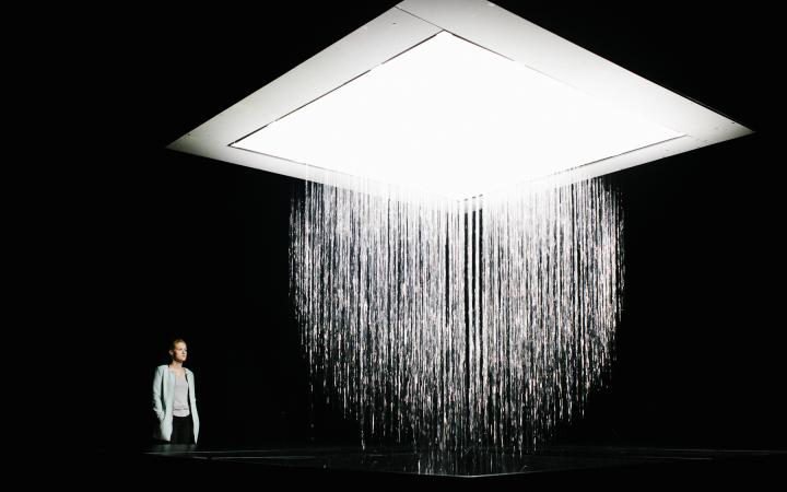Photo of the installation 3D WATERMATRIX in which water falls to the ground and generates 3D shapes. A person is watching the insatallation. 