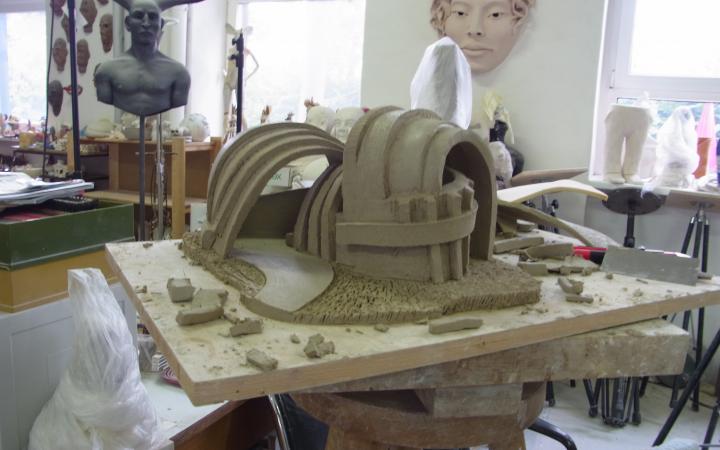 A model of a surrealistic house out of clay is sitting on a panel of wood.
