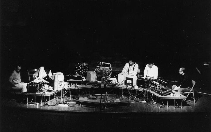 Ein Schwarz-Weiß-Foto der Musikergruppe »The Hub« von 1989, sie sitzen vor einem langen Tisch mit Röhrenbildschirmen und vielen Kabeln.