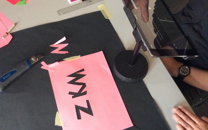 Auf einem Tisch ist das Equipment aufgebaut, welches für Legetrick benötigt wird. Außerdem ein Rosafarbenes Blatt Papier aus dem die Buchstaben ZKM ausgeschnitten wurden.